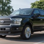 A black 2019 Ford F-150 Limited, popular among Ford trucks for sale, is driving past a lake on a sunny day.