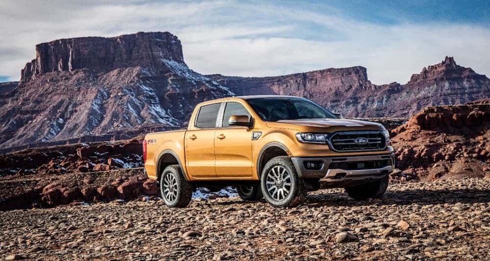 A gold 2019 Ford Ranger, popular among Ford trucks for sale, is parked on rocks with mountains in the background.