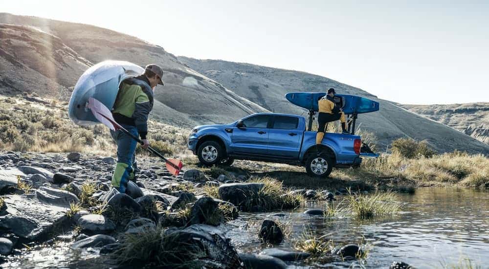 Kayakers are unloading their blue 2019 Ford Ranger at a river edge.