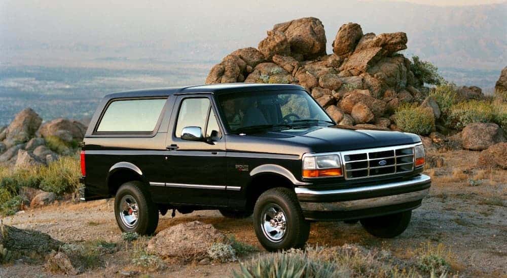 A black 1994 Ford Bronco, which will be reintroduced in Ford's 2020 models, is parked in front of rocks with a view behind it.