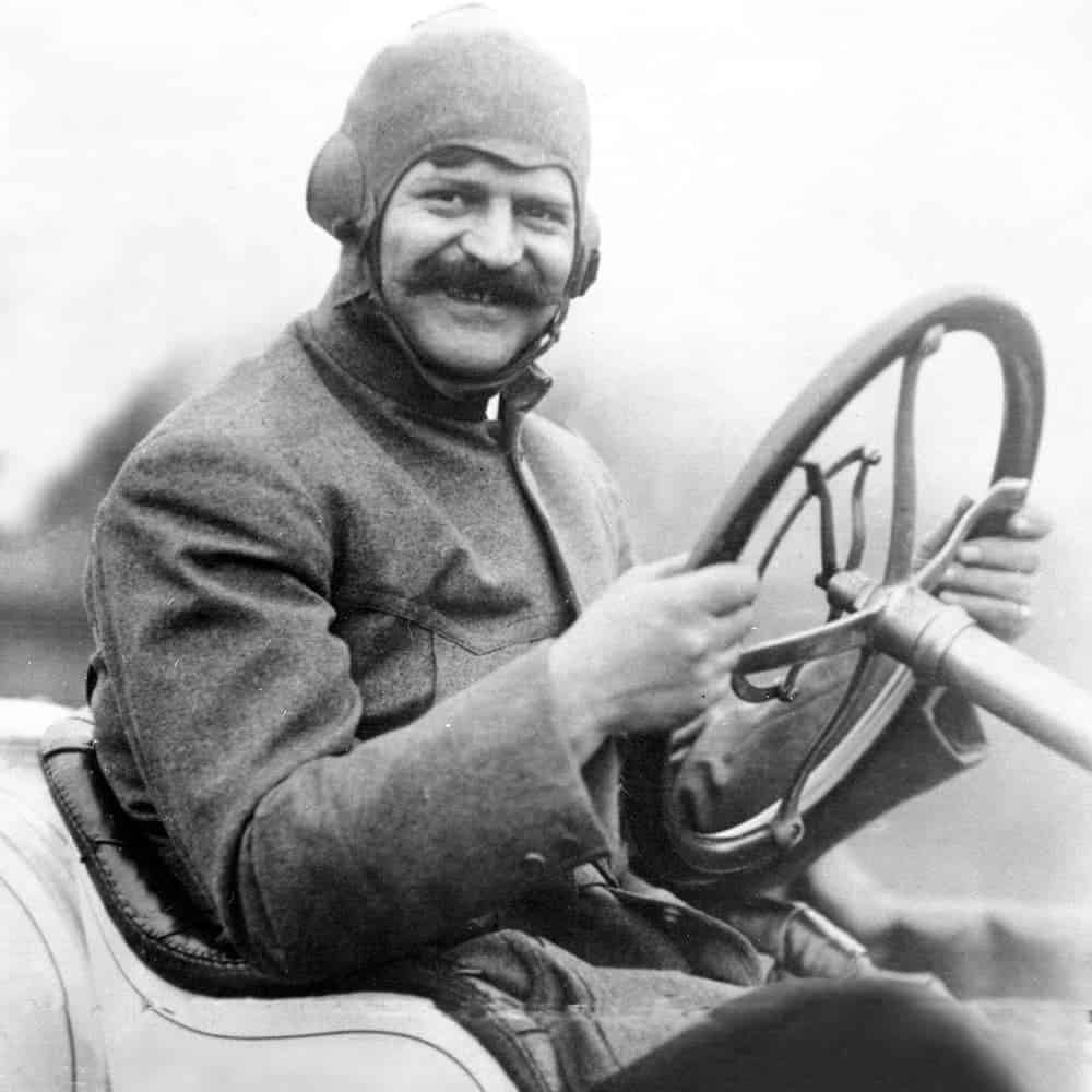 Louis Chevrolet, one of the founders of the brand that lead to the modern Chevy dealership, is shown in black and white at the wheel of a race car in 1911.