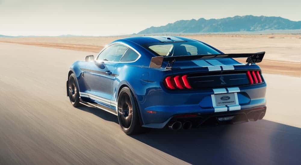 A blue 2020 Ford Mustang Shelby GT500, a new addition to the Ford models, is driving fast on a desert highway.