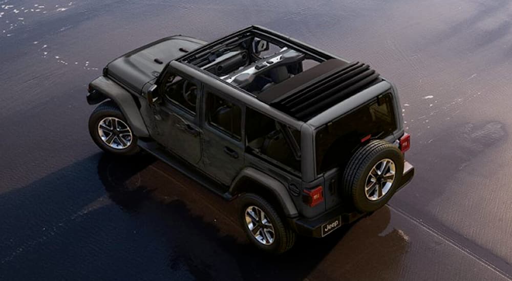 A dark 2019 Jeep Wrangler is in the wet sand of the ocean at the beach.