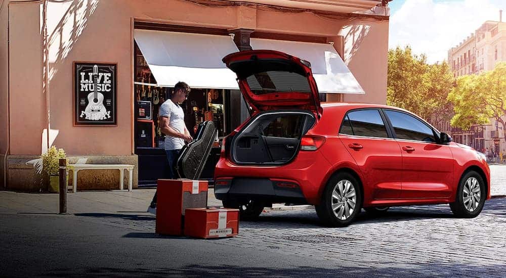 A musician is putting his gear into the back of his 5-door red 2019 Kia Rio.