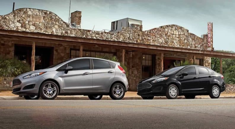 A grey 2019 Ford Fiesta is parked in front of a black Fiesta in front of a stone building.