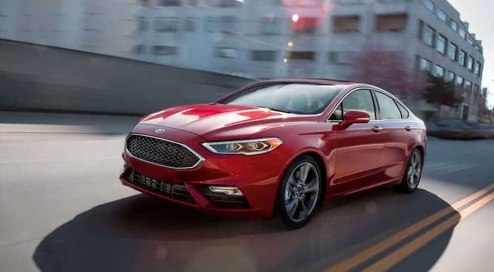 A red 2019 Ford Fusion, a popular new Ford for sale, is driving away from buildings.