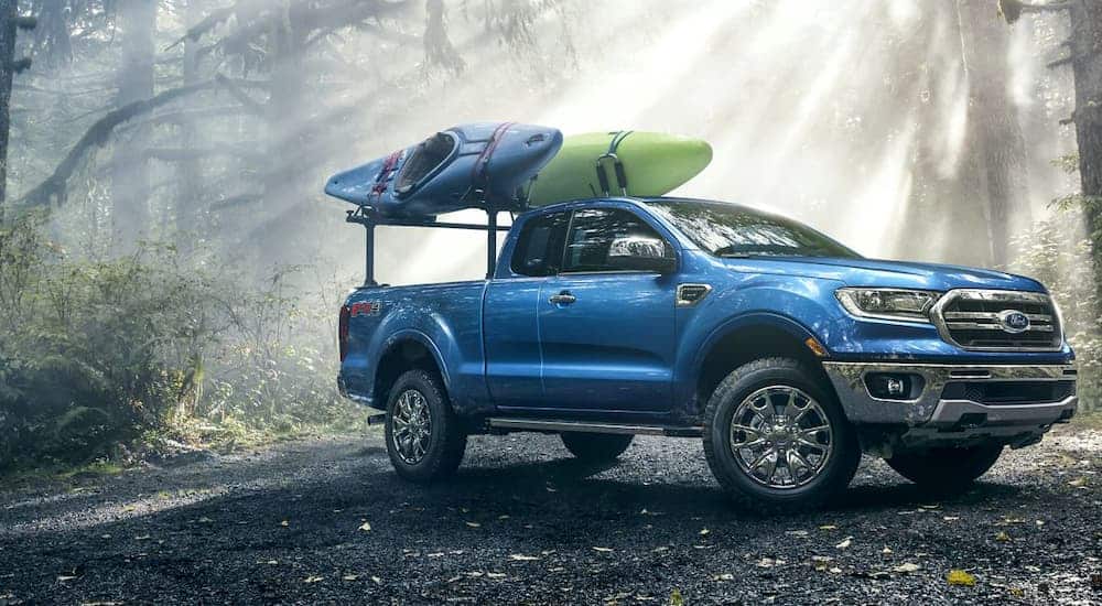 A blue 2019 Ford Ranger, a popular choice for a new Ford for sale, is parked in the woods with kayaks on the bed rack.