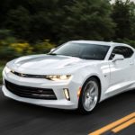 A white 2017 Chevy Camaro is driving on a tree-lined road.