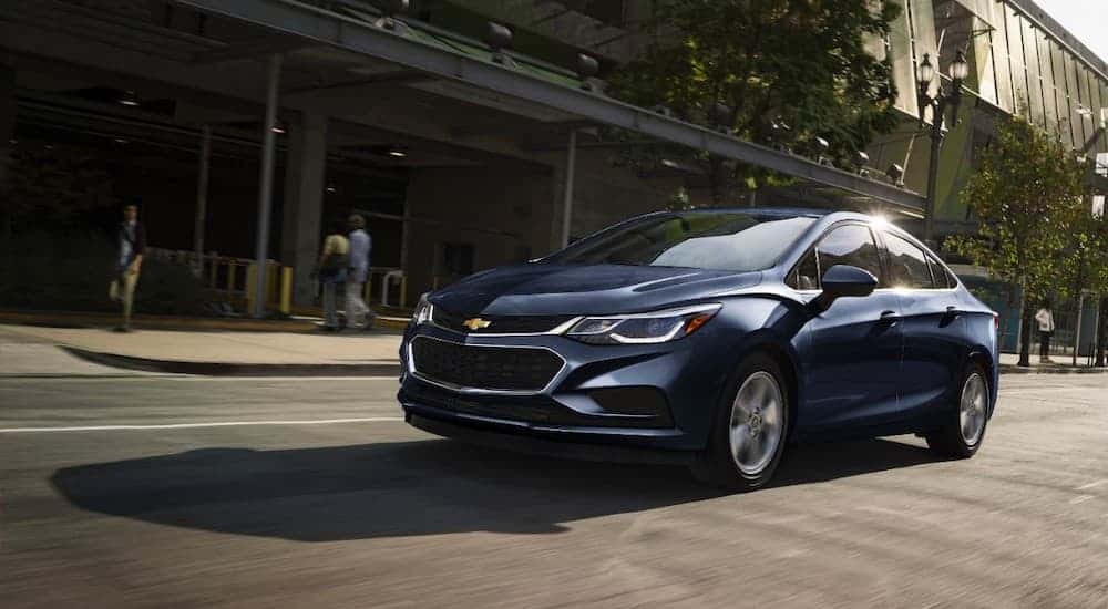 A blue 2017 Chevy Cruze, a popular used Chevrolet car, is driving downtown.