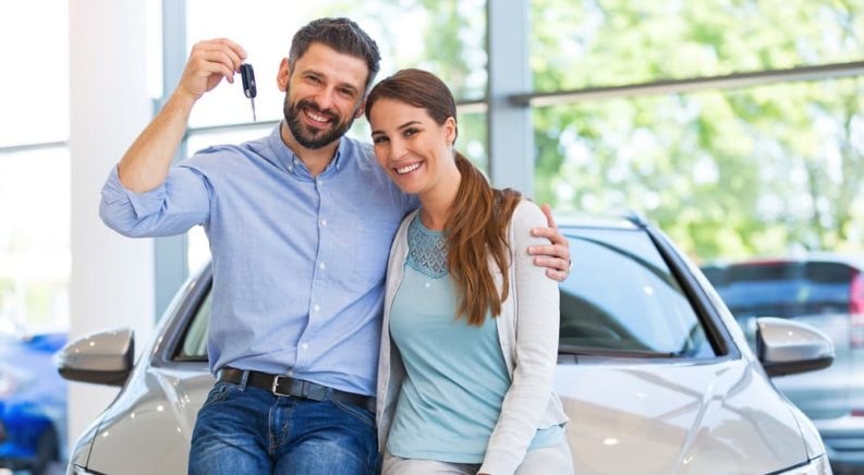 A couple is sitting on their new dream car and holding the keys up.