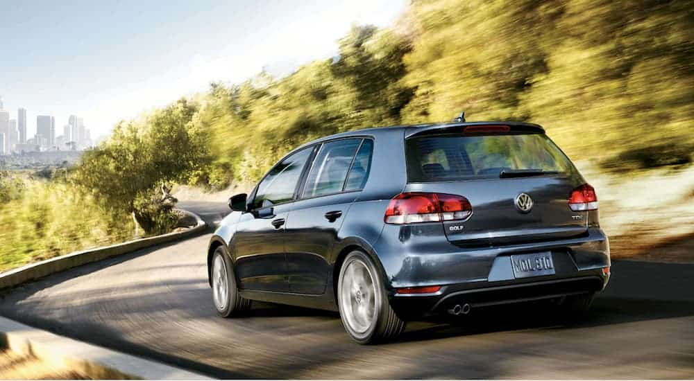 A dark grey 2014 Volkswagen Golf TDI is driving towards a city skyline on a winding road.