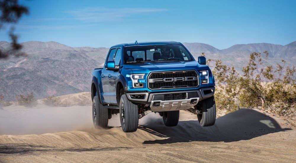 A blue 2019 Ford Raptor is jumping on a trail in the desert.