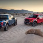 A blue and a red 2019 Ford Raptor are parked in the desert.