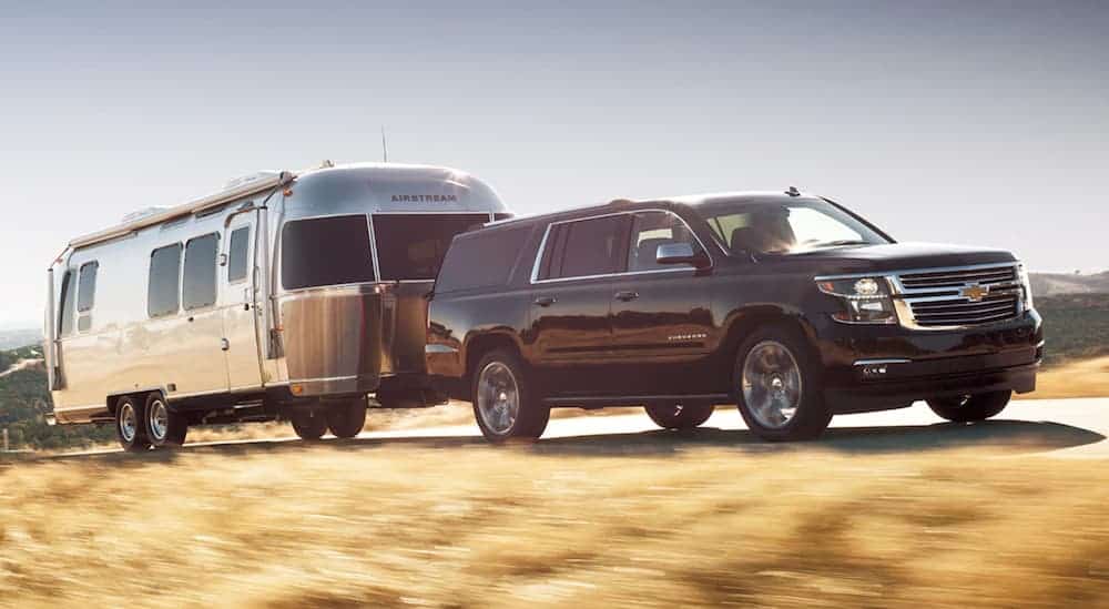 A black 2020 Chevy Suburban is towing an airstream trailer up a hill. 