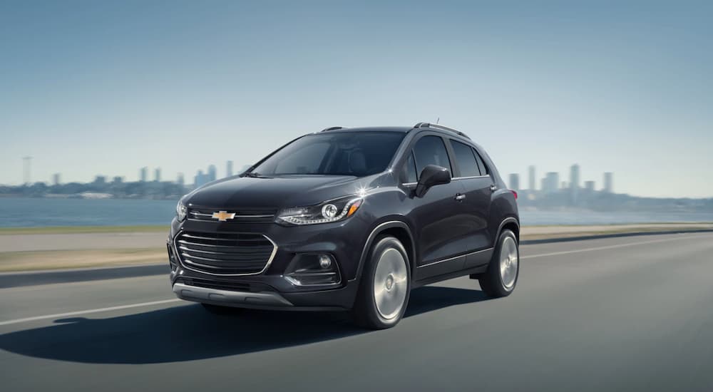 A grey 2020 Chevy Trax is driving away from a city skyline.