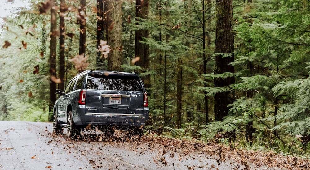 A grey 2020 GMC Yukon is driving through leaves on the road.