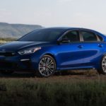 A blue 2020 Kia Forte is in front a field and mountain.