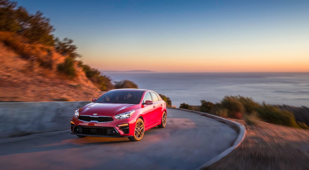 A red 2019 Kia Forte is taking a corner with the ocean in the distance.