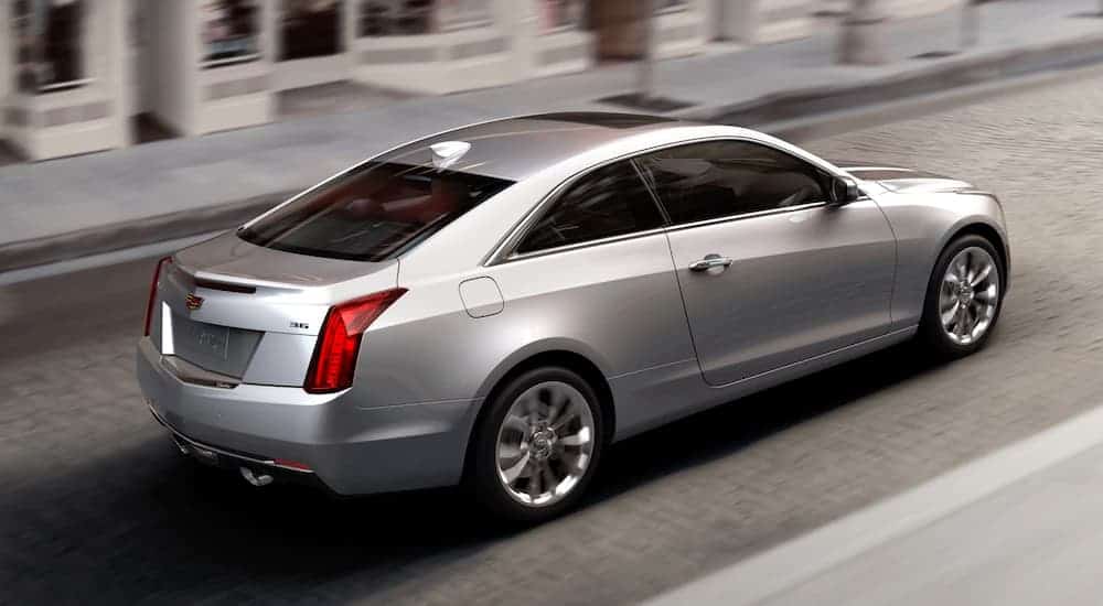 A silver 2019 Cadillac ATS is driving past blurred buildings.