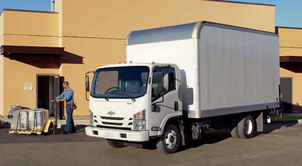 A delivery man is at a loading bay with his white 2019 Chevy Low Cab Forward Truck.