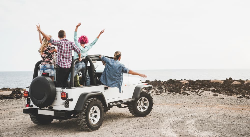 A group of friends are at the beach happily in their topless Jeep Wrangler.