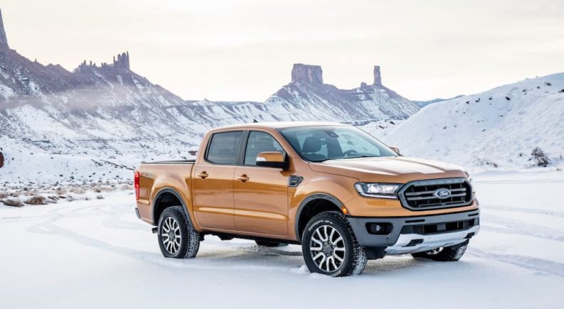 An orange 2019 Ford Ranger is parked in the snow with mountains in the background.