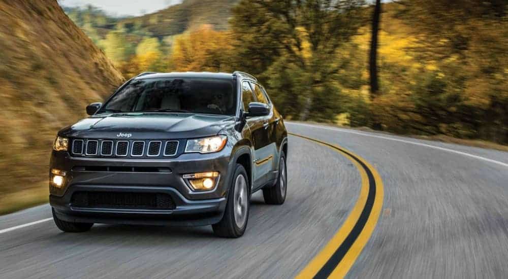 A black 2019 Jeep Compass is driving on a treelined road. 