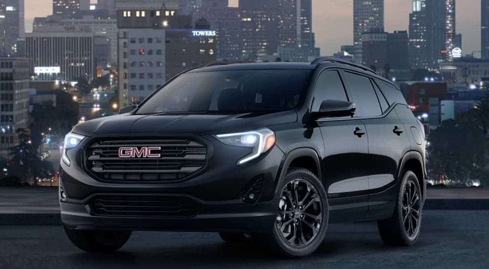 A black 2019 GMC Terrain, which wins when comparing the 2019 GMC Terrain vs 2019 Jeep Compass, is parked at night with city lights behind it.