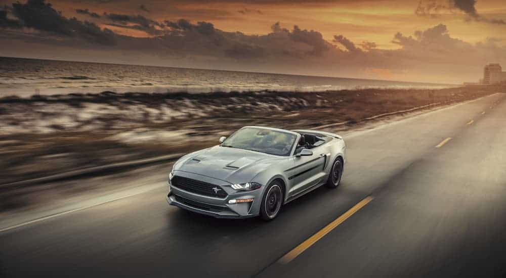 A silver 2020 Ford Mustang convertible is driving on a road at dusk.