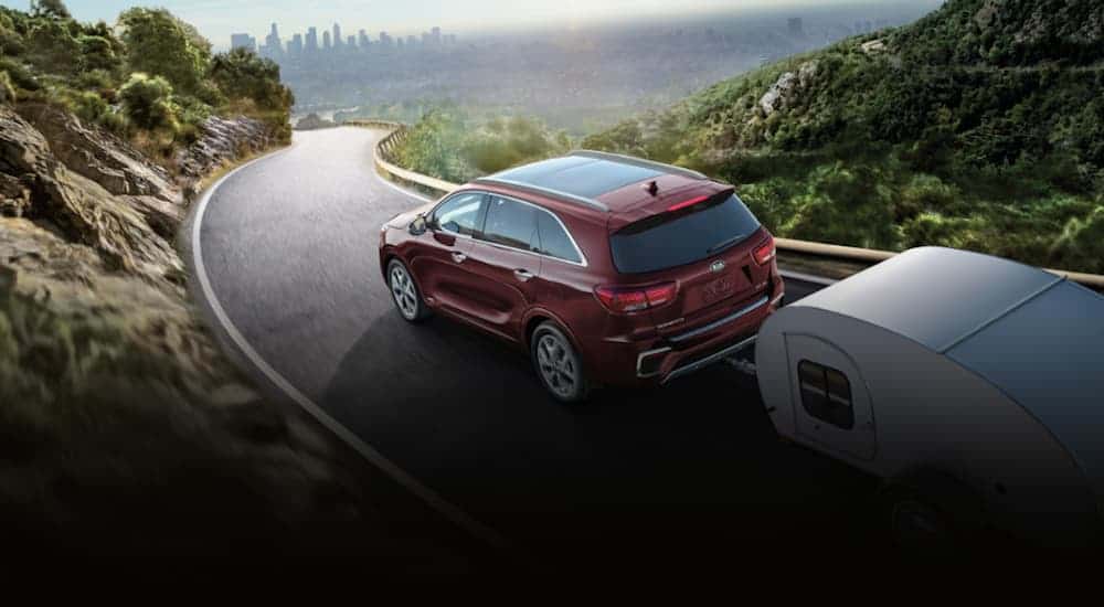 A red 2020 Kia Sorento is towing a camper on a paved mountain road.