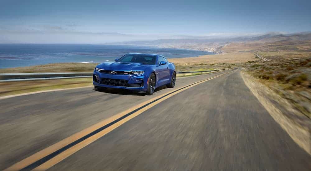 A blue 2020 Chevy Camaro is driving on a highway next to the ocean. 