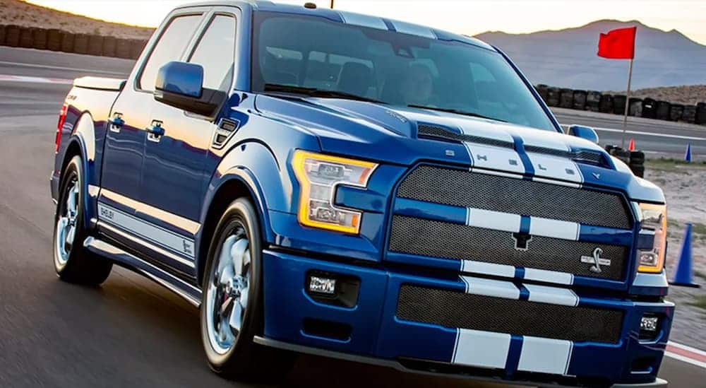 A blue 2017 Ford Shelby F-150 Super Snake is driving on a race track outside of a Ford dealership. 