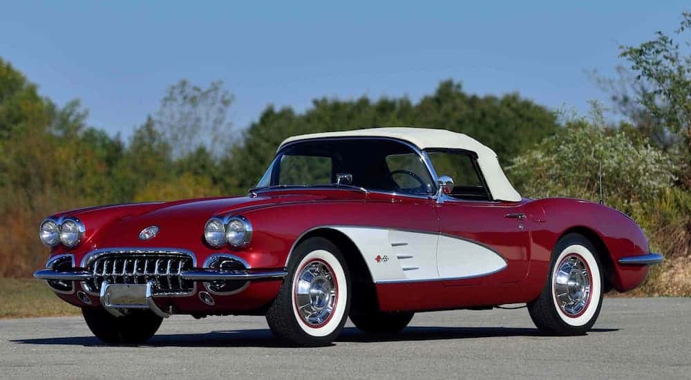 A red 1960 Chevrolet Corvette is parked in an empty treelined parking lot.