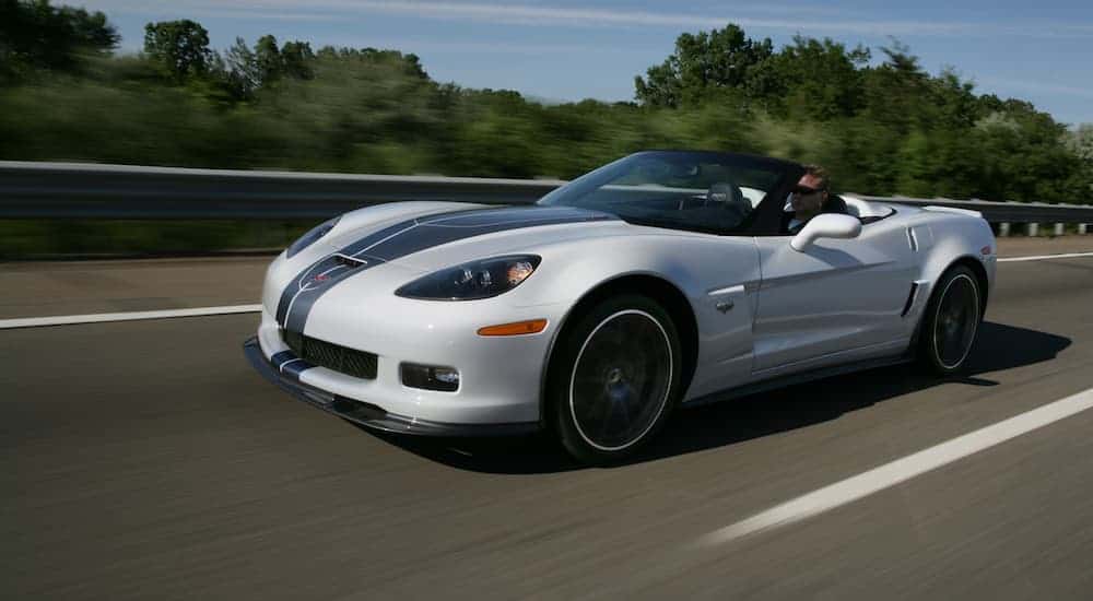 A white 2013 Chevy Corvette convertible, popular among used cars with great performance, is driving on an empty highway.