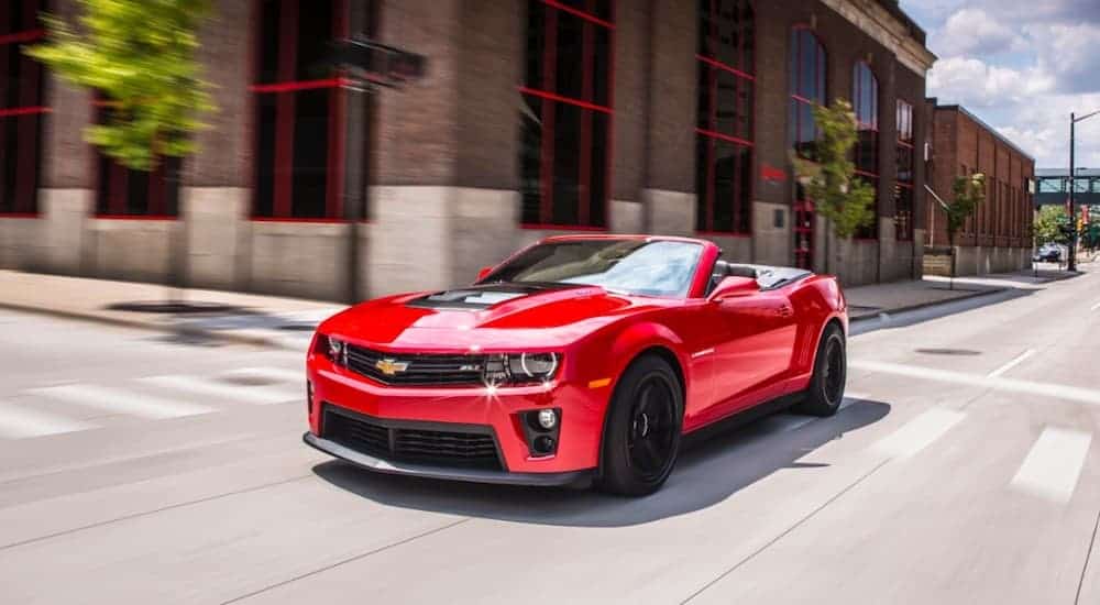 A red 2013 Chevy Camaro Convertible is driving on a city street. 
