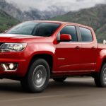 A red 2020 Chevy Colorado is towing dirt bikes with mountains in the background.