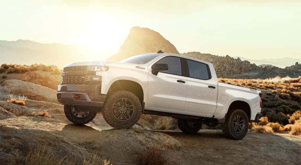 A white 2020 Chevy Silverado 1500 Custom Trail Boss is rock crawling in the desert with a sun glare on it.