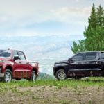 Two 2020 Chevy Silverado 1500's are parked in a grassy field with mountains in the background.