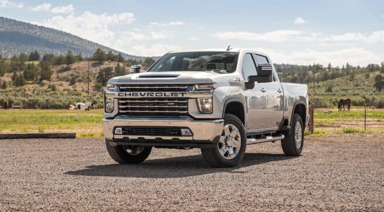 A white 2020 Chevy Silverado HD is parked in a dirt parking lot with grassy mountains in the background.