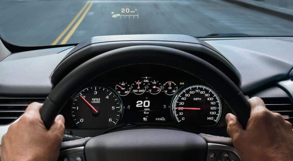 Hands are on the steering wheel of the 2020 Chevy Tahoe showing the 8-inch screen displaying driver information and the Heads-Up Display.