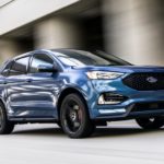 A blue 2020 Ford Edge ST is driving on a highway.