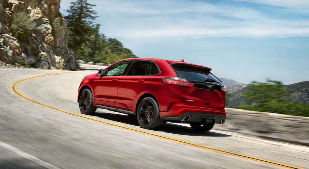 A red 2020 Ford Edge ST is driving uphill and around a corner.