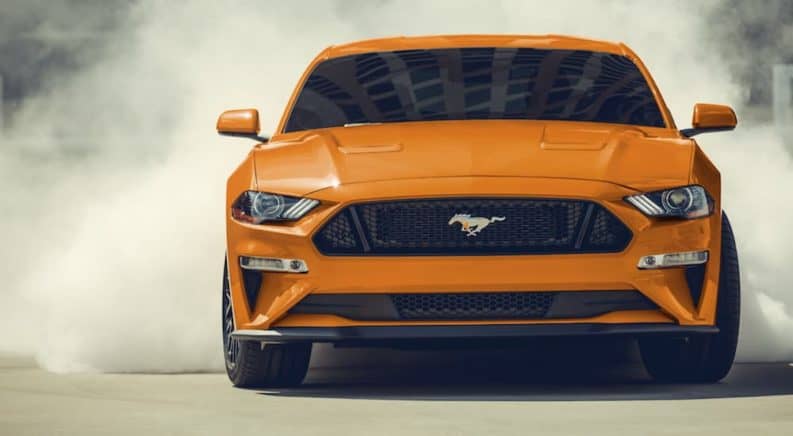 An orange 2020 Ford Mustang is doing burn outs in a parking lot.