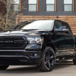 A black 2020 Ram 1500, which wins when comparing the 2020 Ram 1500 vs 2020 Ford F-150, is parked in front of a wooden wall next to a house.
