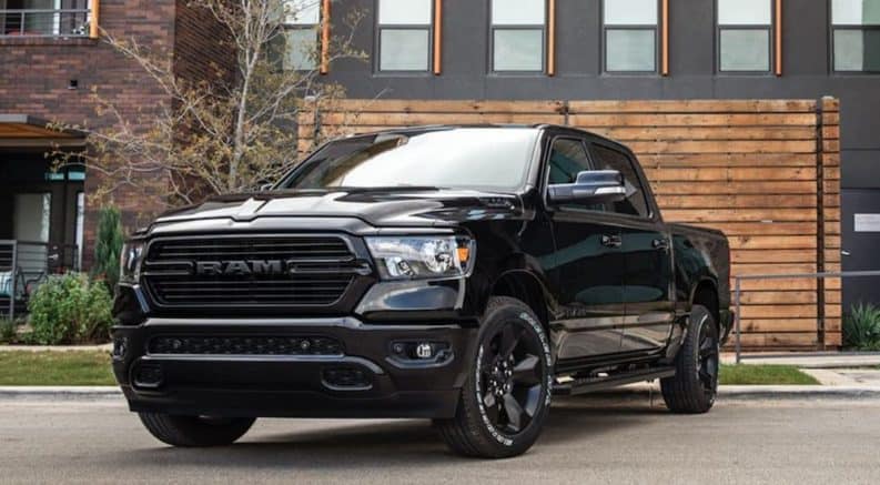 A black 2020 Ram 1500, which wins when comparing the 2020 Ram 1500 vs 2020 Ford F-150, is parked in front of a wooden wall next to a house.