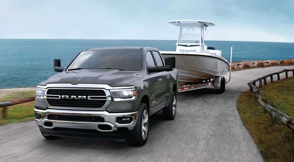 A grey 2020 Ram 1500 is towing a large boat next to the ocean. 
