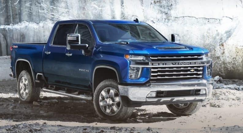A blue 2020 Chevy Silverado 2500 HD is parked in front of a rock wall near a Chevy dealership.