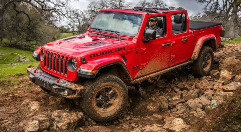 A red 2020 Jeep Gladiator Rubicon is rocking on rocks with mud on the fenders.