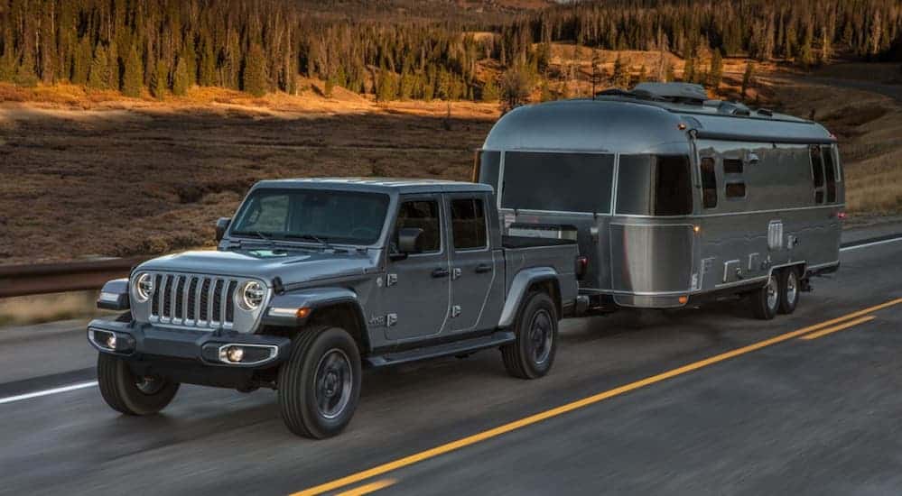 A silver Jeep Gladiator Overland Edition is towing a large Airstream trailer on a desert road.