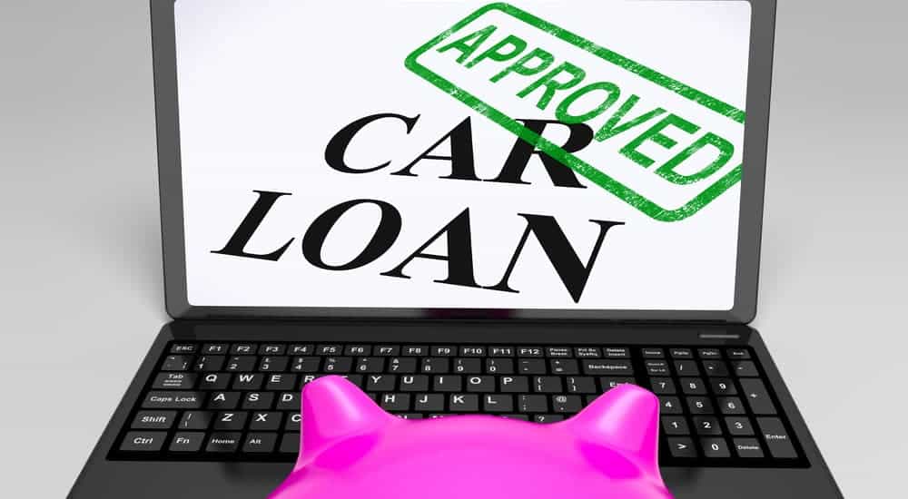 A piggy bank is looking at a laptop that says, 'Car Loan Approved'.